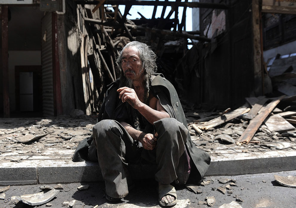 Мужчина сиди перед разрушенным зданием в уезде Лушань
