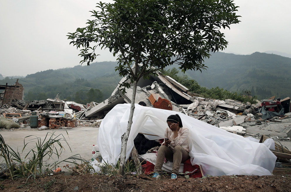 Девочка сидит возле разрушенных домов в деревне Лунмэнь