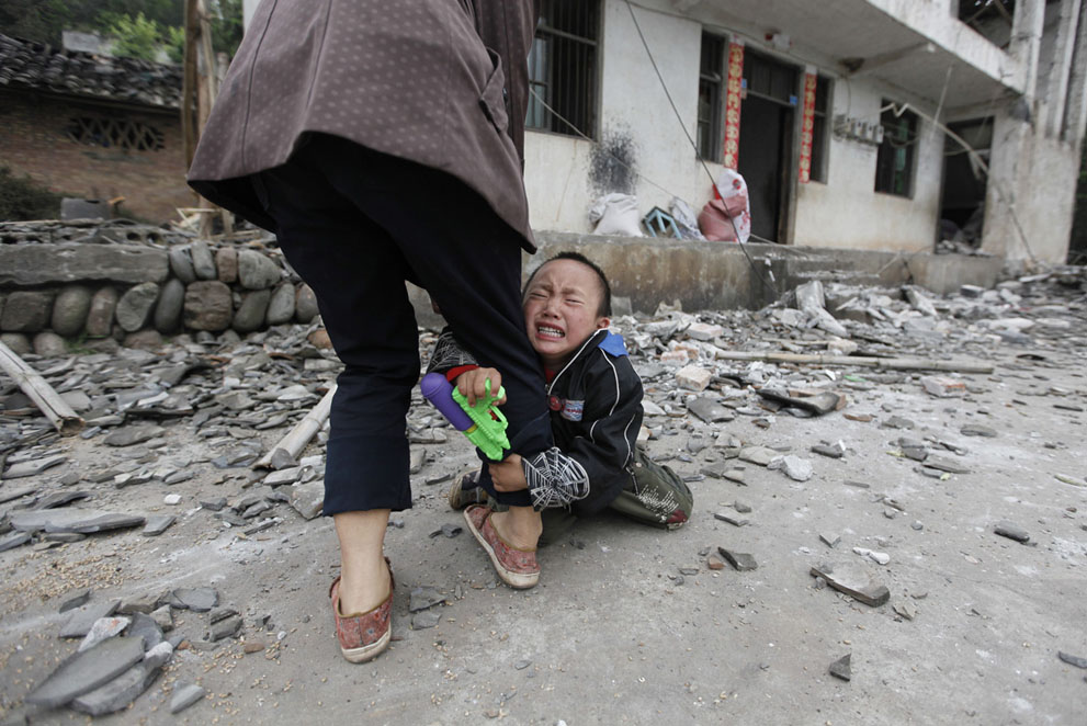 Ребенку страшно. Мальчик держит за ногу свою мать перед их разрушенным домом в деревне Лунмэнь, уезд Лушань